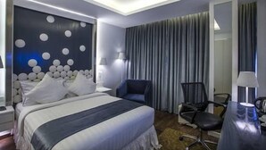 A hotel room with a large bed, a desk with a chair, a wall with circular patterns, and a large window with curtains. - Hotel Grace 21 (Dhaka)