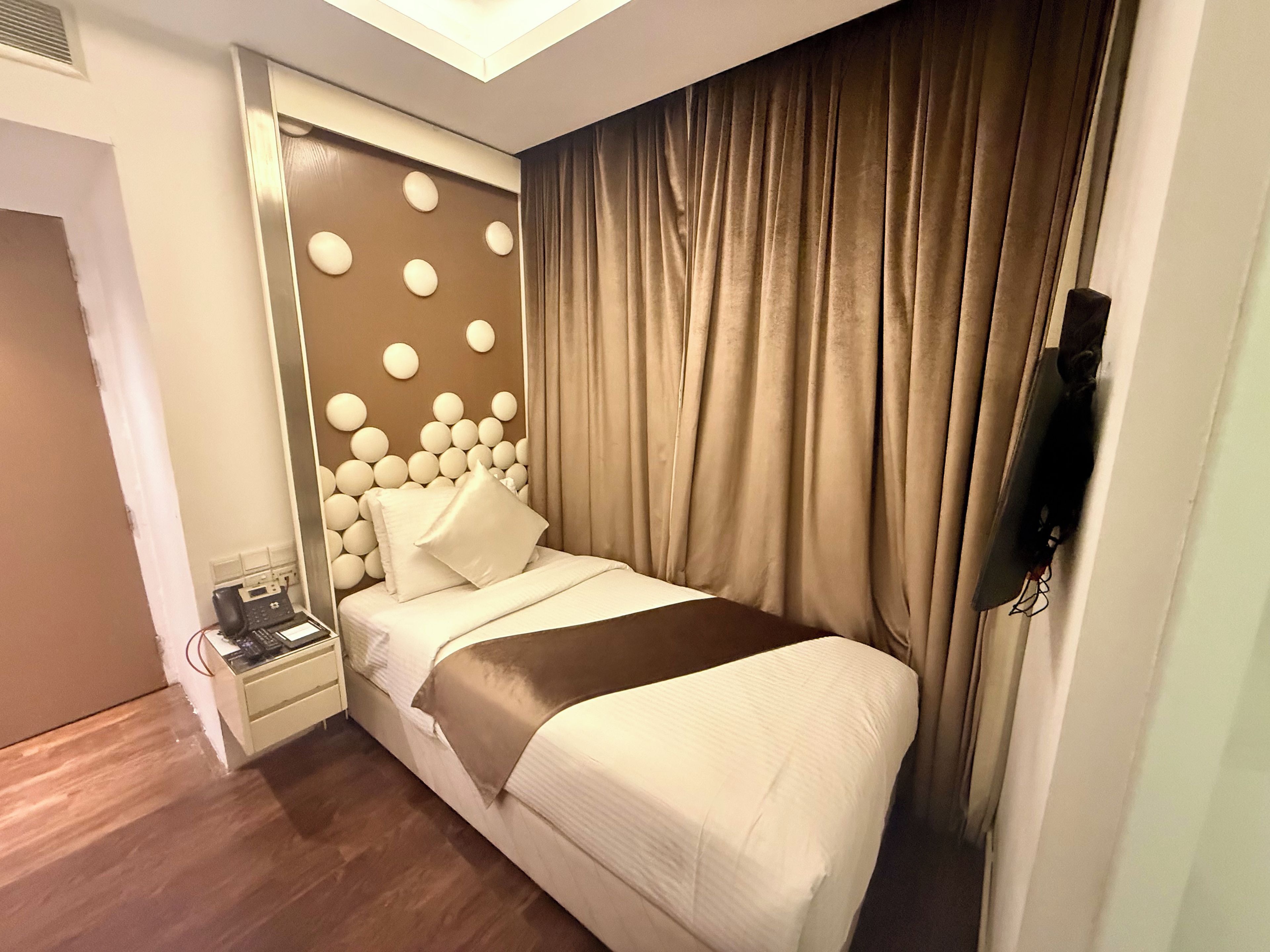 A hotel room with a bed, a bedside table, a telephone, and a wall-mounted TV.
