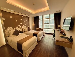 Habitació d'hotel amb dos llits, una taula de treball, televisió i una finestra gran.