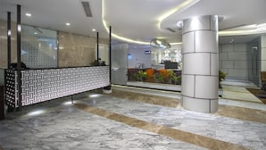 A modern reception area with a patterned reception desk, a large column, and a decorative wall with plants. - Hotel Grace 21 (Dhaka)