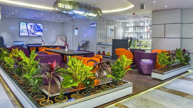 A modern hotel lobby with a seating area, a TV screen, and a display case with food items. - Hotel Grace 21 (Dhaka)