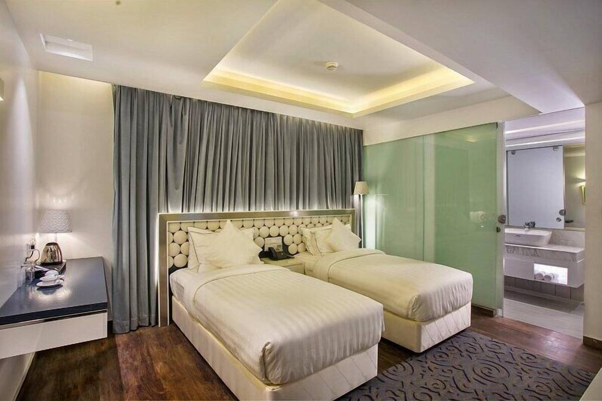 A hotel room with two beds, a desk, a mirror, and a bathroom with a sink and mirror.