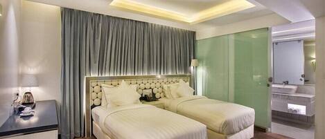 A hotel room with two beds, a desk, a mirror, and a bathroom with a sink and mirror.