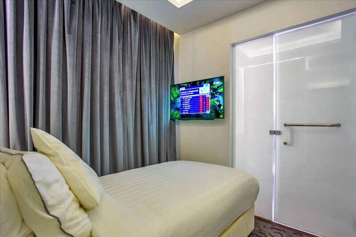 A hotel room with a bed, a television mounted on the wall, and a door.