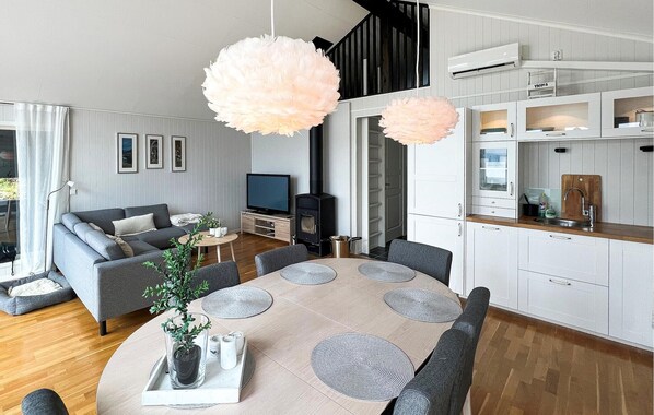 A modern living room with a grey sofa, a TV, and a fireplace. There is a dining area with a table and chairs, and a kitchen with white cabinets and a wooden countertop.