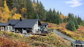 Eine Hütte mit einer Terrasse, umgeben von Wald und Herbstlaub.