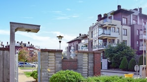 Zona residencial con modernos edificios de apartamentos, un acceso con reja y una calle con coches estacionados.