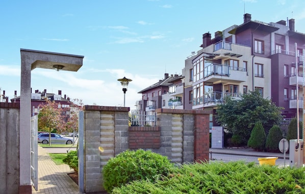 Zona residencial con modernos edificios de apartamentos, un acceso con reja y una calle con coches estacionados.