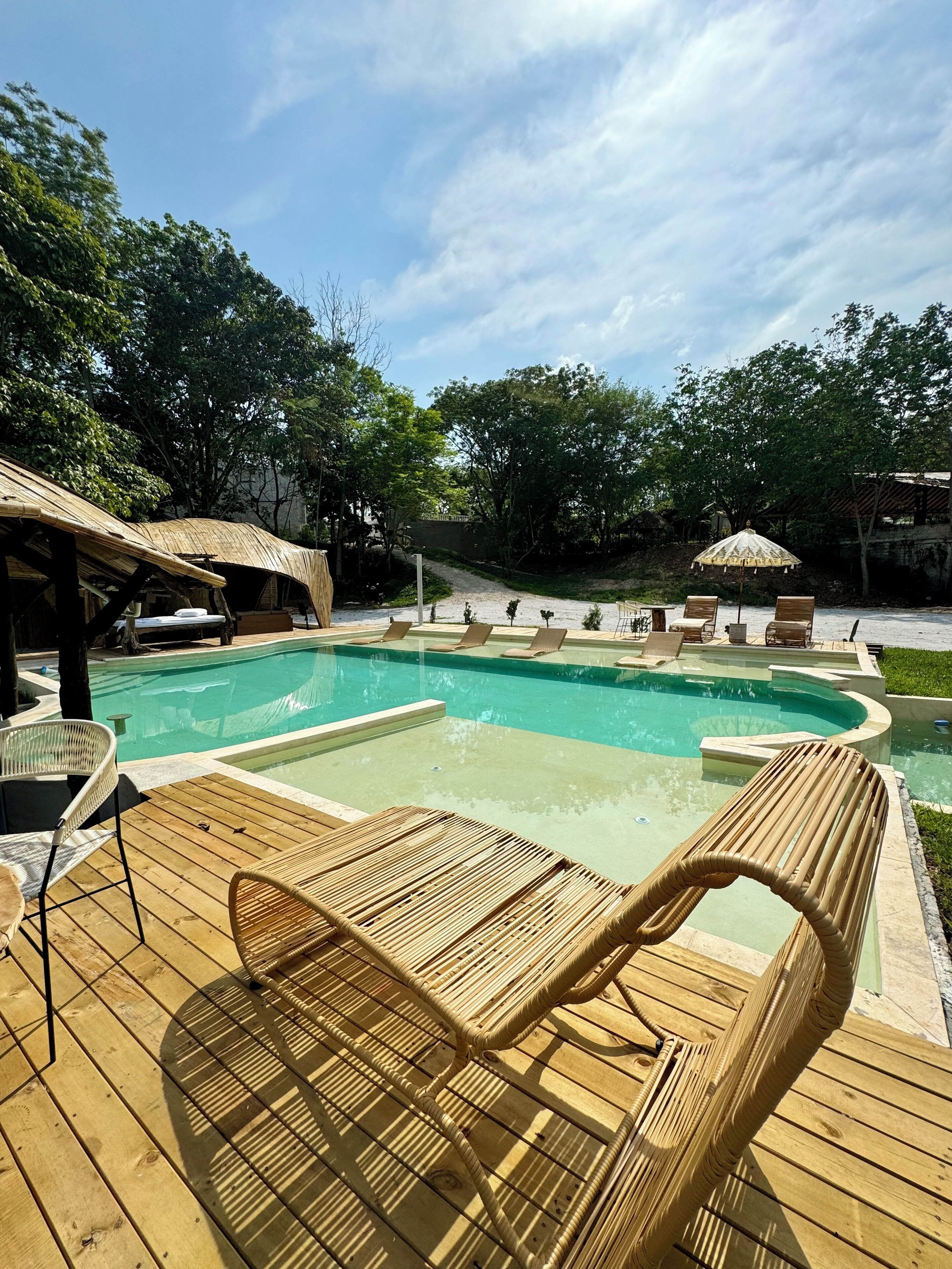 Ein Poolbereich mit Holzterrasse, Liegestühlen und Sonnenschirmen.