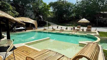 Ein Poolbereich mit Holzterrasse, Liegestühlen und Sonnenschirmen.