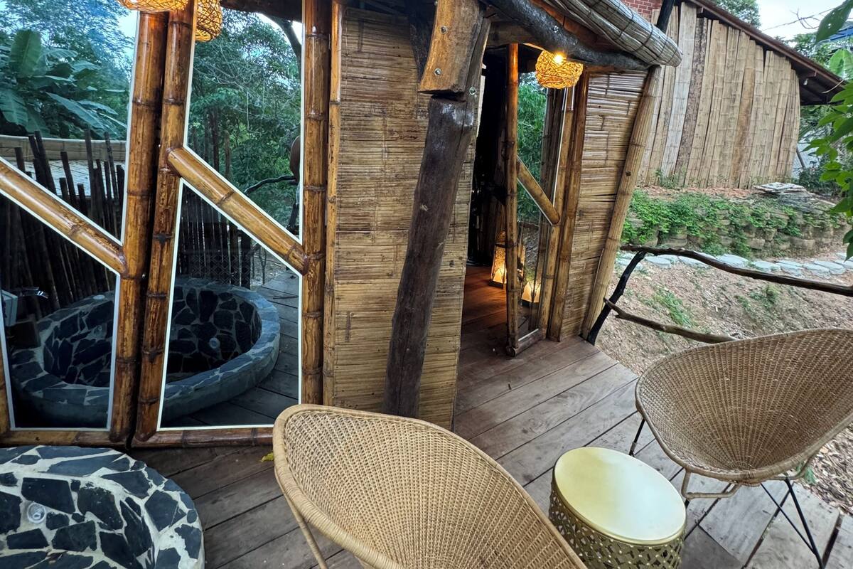 A rustic wooden cabin with a stone-tiled patio, wicker furniture, and a stone fireplace.