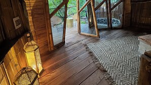 A wooden interior with a large mirror, a woven rug, and a view of greenery outside. - Akasha suites (Puerto Triunfo)