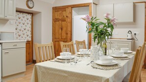 A dining area with a table set for four, wooden chairs, a vase with flowers, and a clock on the wall. - 3 bedroom accommodation in Blairgowrie (Blairgowrie)