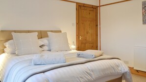 A neatly made bed with white linens and pillows, a wooden door, and a radiator on the wall. - 3 bedroom accommodation in Blairgowrie (Blairgowrie)