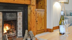 A cozy room with a fireplace, wooden cabinet, and a table with a wine bottle and glasses. - 3 bedroom accommodation in Blairgowrie (Blairgowrie)