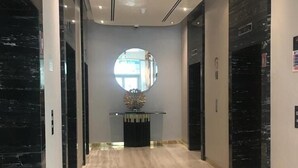 A modern hallway with a marble floor, a round mirror, and black elevator doors. - Damac Majestine VIP (Dubai)
