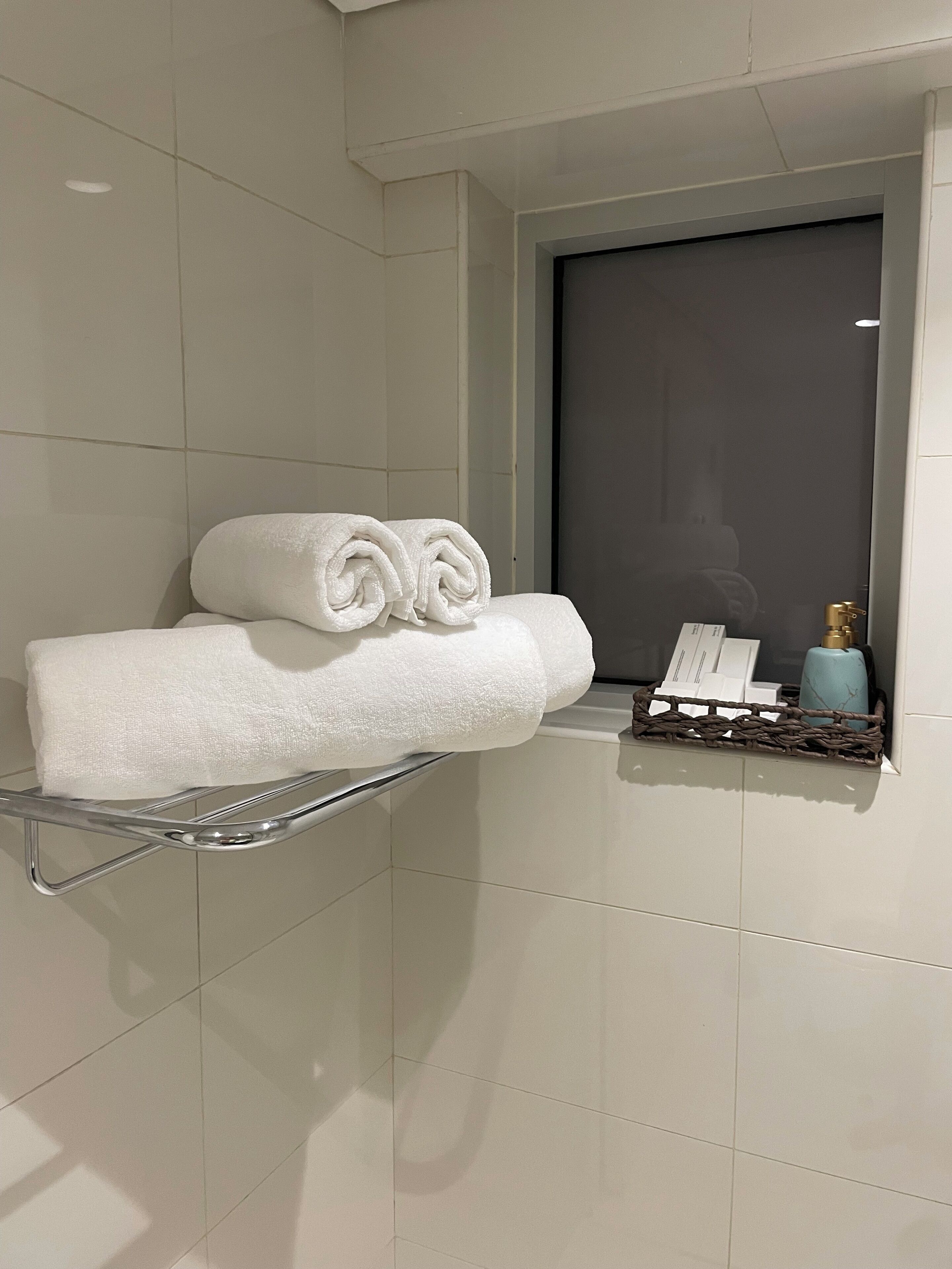 Un bagno con un portasciugamani che contiene due asciugamani arrotolati, un piccolo ripiano con articoli da toilette e una porta di colore scuro.