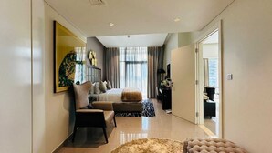 A modern hotel room with a large bed, a sitting area with a chair and ottoman, a desk, and a large mirror. - Damac Majestine VIP (Dubai)