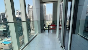 A balcony with a glass railing, a tiled floor, and a view of high-rise buildings. - Damac Majestine VIP (Dubai)