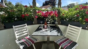 Een terras buiten, met een tafel en stoelen, omgeven door weelderige begroeiing en bloemen.