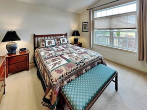 A bedroom with a large bed, a bench, two bedside tables, and a window with curtains. - Westwind by Taylor Made Deep Creek (McHenry)