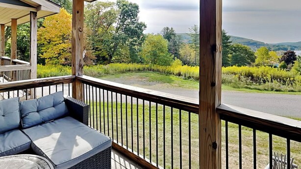 A covered porch with a blue cushioned seating area and a view of a landscaped garden and road. - Bluebeary Retreat by Taylor Made Deep Creek (McHenry)