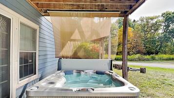 A hot tub with a safety warning sign, a wooden pergola, and a house with blue siding.