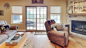A living room with a fireplace, leather sofas, a coffee table, and a large window with blinds. - Bluebeary Retreat by Taylor Made Deep Creek (McHenry)
