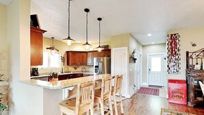 A kitchen with wooden bar stools, a stainless steel refrigerator, and pendant lighting. - Bluebeary Retreat by Taylor Made Deep Creek (McHenry)