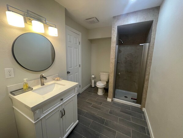 A bathroom with a white vanity, a round mirror, a toilet, and a glass-enclosed shower.