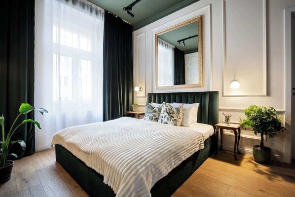 Une chambre d’hôtel avec un grand lit, un miroir, une table de chevet et une plante en pot.