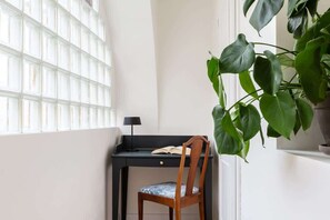Een bureau in de hoek met een stoel, een bloempot en een raam met jaloezieën.
