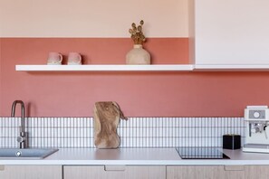 A kitchen counter with a sink, a coffee machine, and a vase with dried flowers on a shelf.