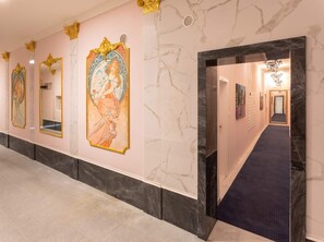 Un pasillo con paredes de mármol, molduras doradas decorativas y una serie de obras de arte enmarcadas.