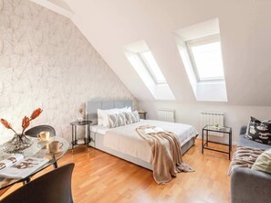 Un dormitorio estilo loft moderno con techo inclinado, una cama grande, una mesita pequeña y una zona de estar acogedora.