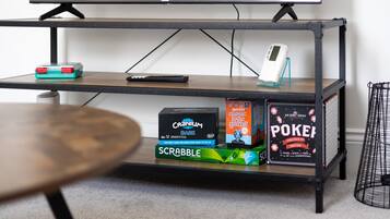 Ein TV-Schrank mit Fernbedienung, einer Digitaluhr und Gesellschaftsspielen wie Scrabble und Pictionary.