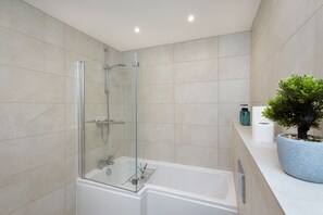 A modern bathroom with a glass-enclosed shower, a white bathtub, and a potted plant on the countertop.