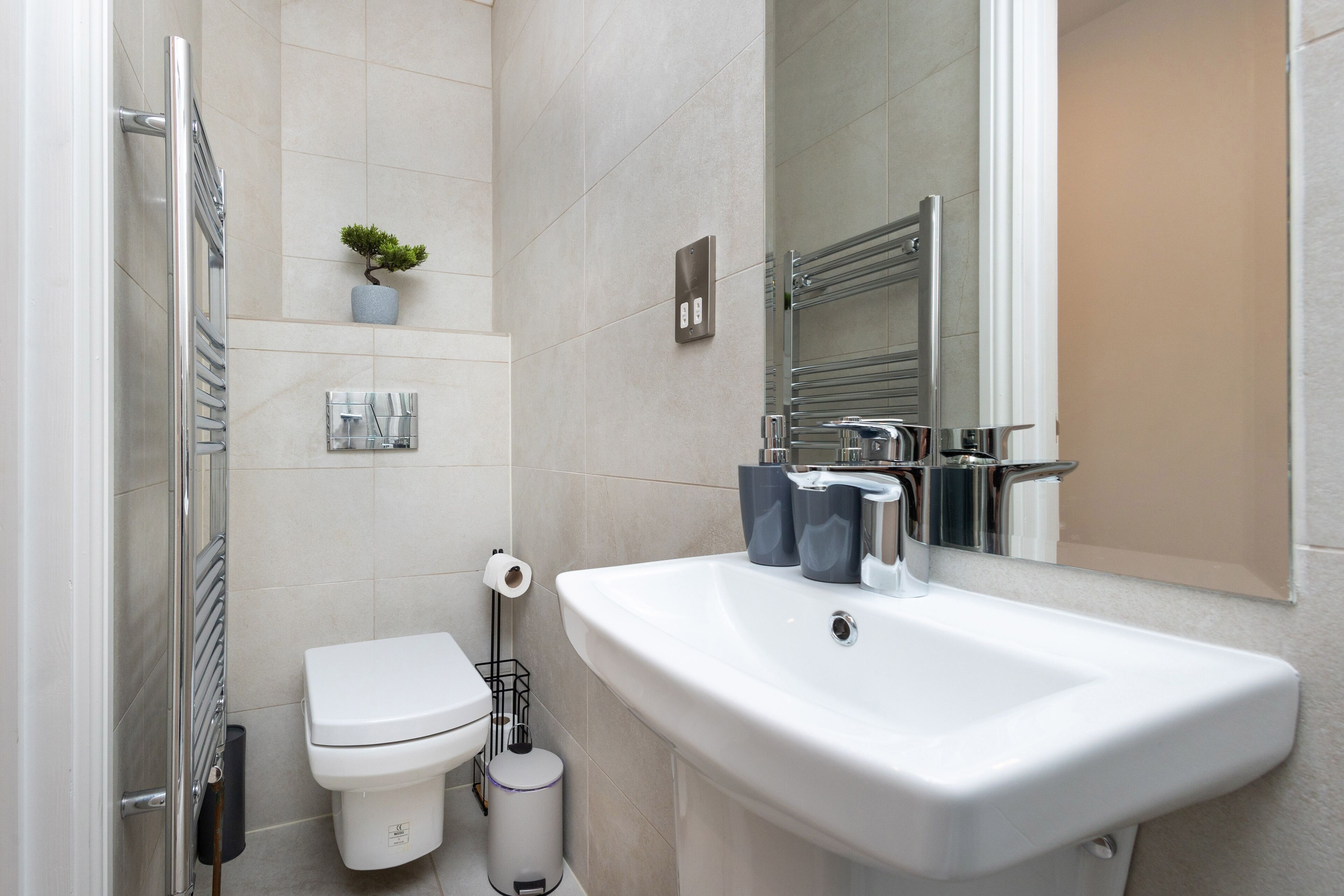 Un baño moderno con lavamanos blanco, inodoro, perchero y una pequeña planta en maceta.