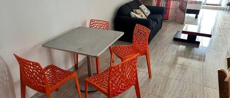 A dining area with a table and four orange chairs, a black sofa, and a red telephone booth decoration on the wall.