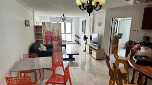 Un salón amplio con comedor, cocina y vistas a un edificio rojo a través de un ventanal grande.