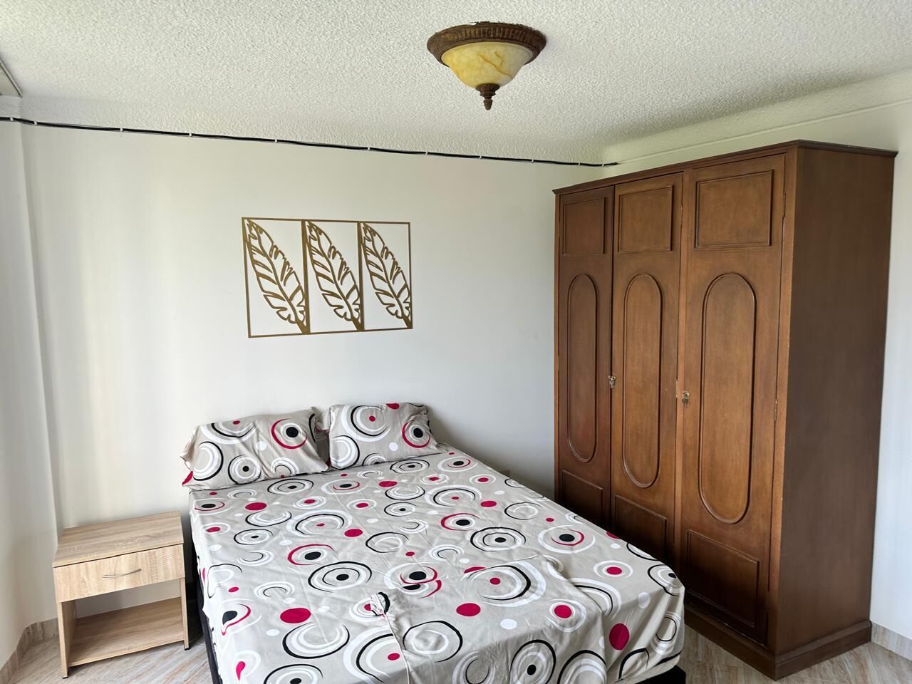 Un dormitorio con cama, armario, mesita de noche y una obra de arte en la pared.