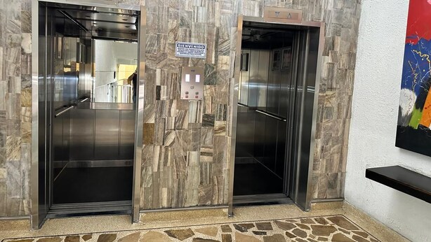 Dos puertas de ascensor con diseño de pared de piedra, un cartel de bienvenida y un panel de control.