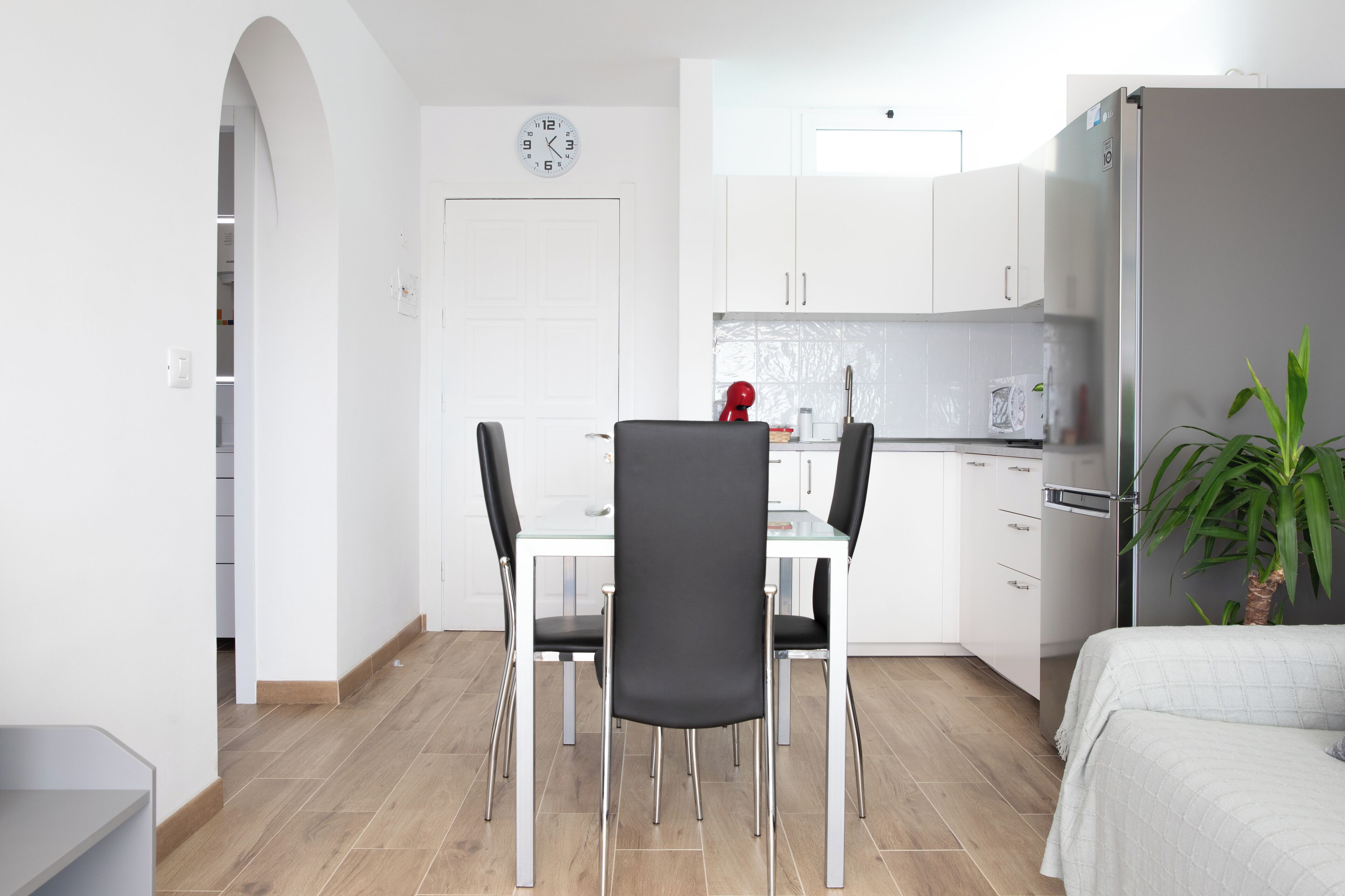 Une cuisine moderne avec des meubles blancs, un réfrigérateur en acier inoxydable et un coin repas comprenant une table en verre et des chaises noires.