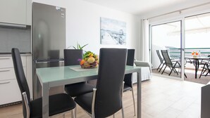Un espace repas moderne avec une table en verre, des chaises noires et un saladier rempli de fruits.