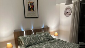 A neatly arranged bedroom with a bed, two bedside tables, a wall clock, and a framed artwork. -  Carre D’Or - Discover a unique address in the heart of Promenade des Anglais.  (Nice)