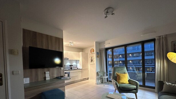 A modern living room with a flat-screen TV, a sofa, a coffee table, and a dining area with a kitchen in the background. -  Carre D’Or - Discover a unique address in the heart of Promenade des Anglais.  (Nice)