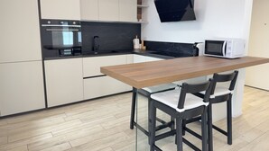 Een moderne keuken met witte kasten, een zwart aanrecht, een houten tafel en twee zwarte stoelen.