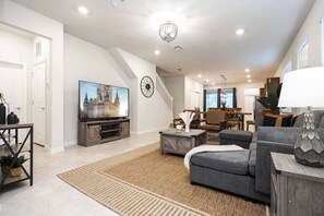 A spacious living room with a large flat-screen TV, a staircase, and a dining area.
