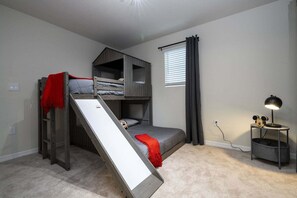 Uma cama beliche com escada, uma escrivaninha com luminária e uma janela com cortinas.