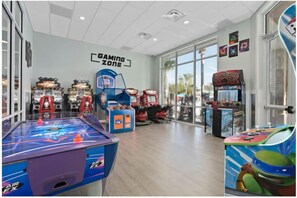 Espaço de jogos coberto com diversas máquinas de arcade, uma mesa de pingue-pongue e um letreiro indicando 'Gaming Zone'.